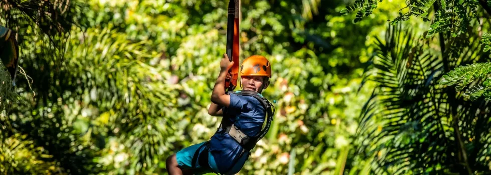 Child zipline guest holds on while flying over jungle