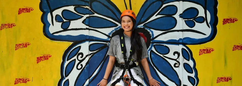 Zipline customer in harness poses in front butterfly mural