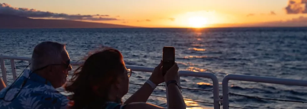 Tourists photograph sunset during maui dinner cruise