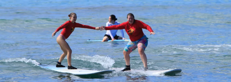 Friends hold hands while waikiki surf lesson