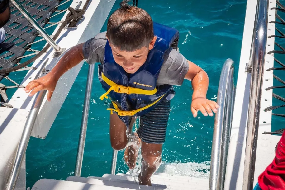 Kid using stairs to board catamaran from water outside of Waikiki